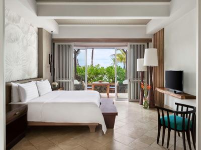 Lichte hotelkamer met tweepersoonsbed, bureau en terras met uitzicht op palmbomen.