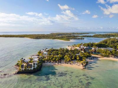 Luftaufnahme einer Küstenlandschaft mit Strand, Bäumen und Häusern unter blauem Himmel.