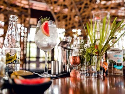 Een bar met verschillende dranken, glazen en plantenversiering op een houten aanrecht.