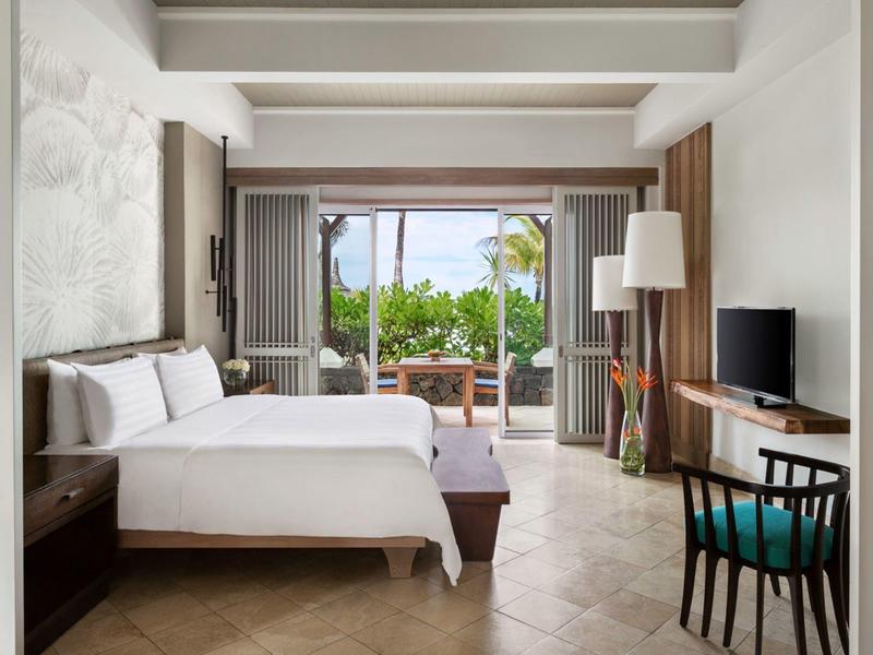 Lichte hotelkamer met tweepersoonsbed, bureau en terras met uitzicht op palmbomen.