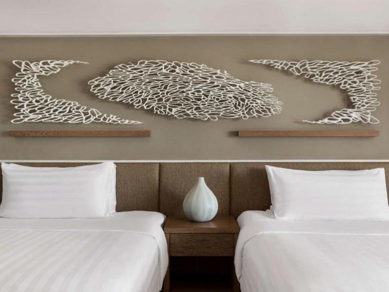 Hotelkamer met twee eenpersoonsbedden, nachtkastje en decoratieve wandkunst boven de bedden.