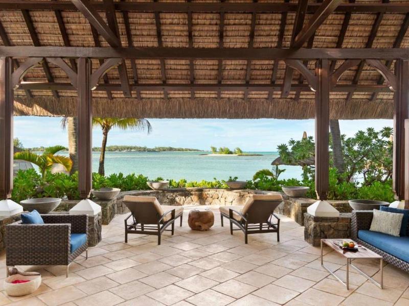 Open lounge met comfortabele stoelen en uitzicht op zee onder een houten dak.