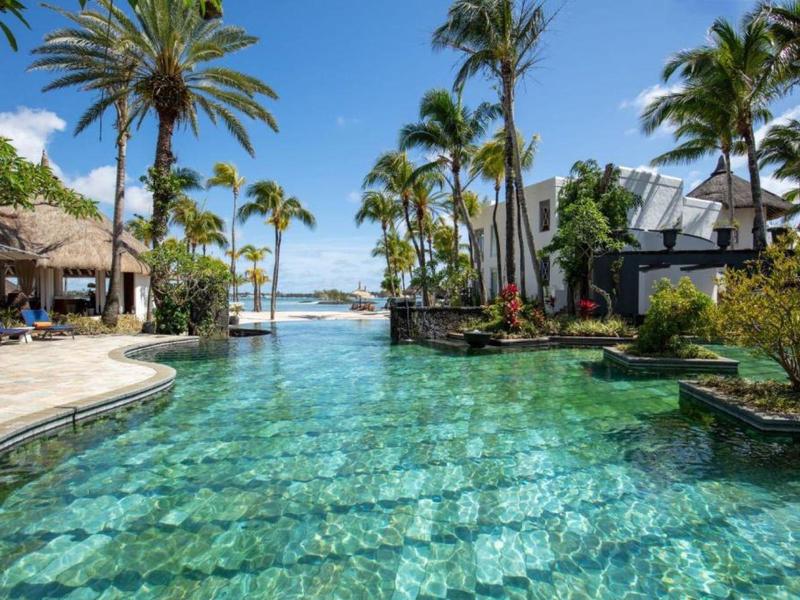 Groot zwembad met palmbomen en uitzicht op zee bij een tropisch hotelresort.