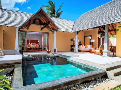 Moderner Bungalow mit L-förmigem Pool, Holzterrasse, bequemen Sofas und tropischer Bepflanzung.