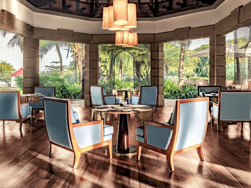 Bright modern restaurant with blue chairs and large windows overlooking palm trees.