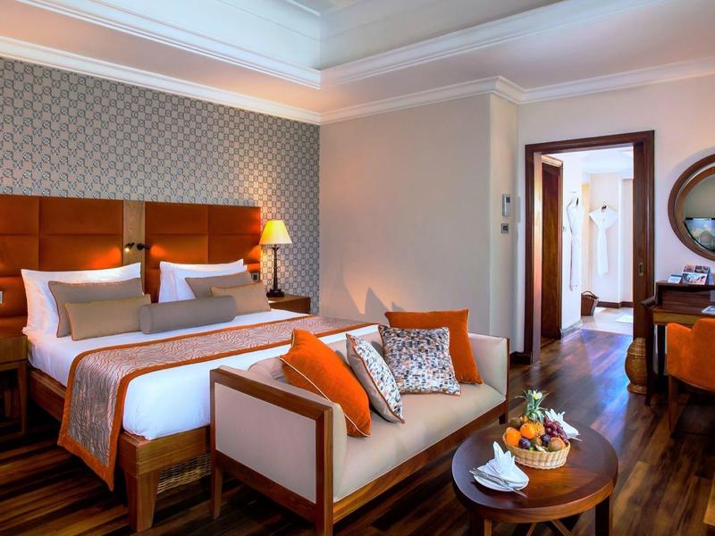 Elegant hotel room with double bed, sofa, wooden floor, and stylish lighting.