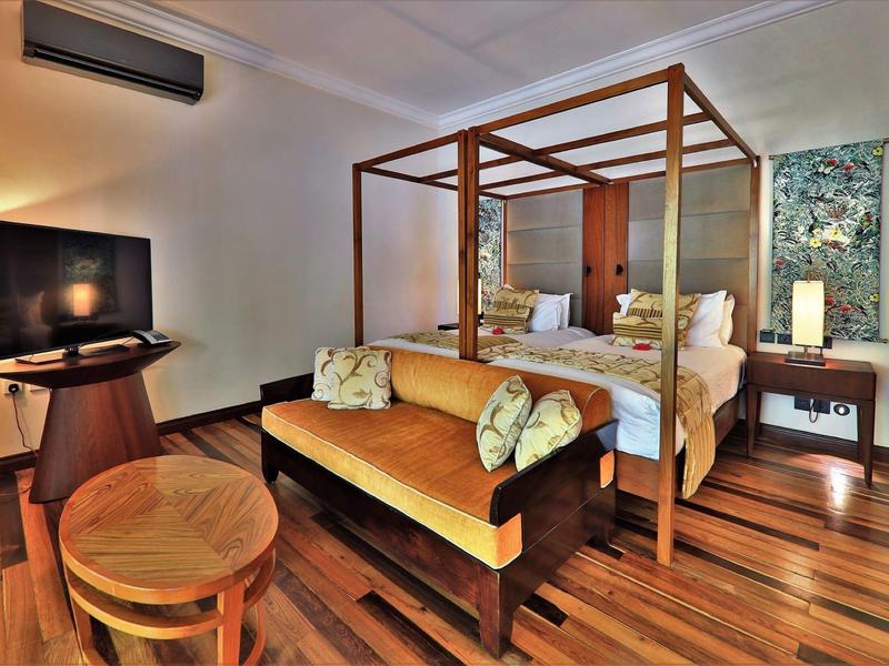 Modern hotel room with wooden chair, sofa, and canopy bed on hardwood floor.