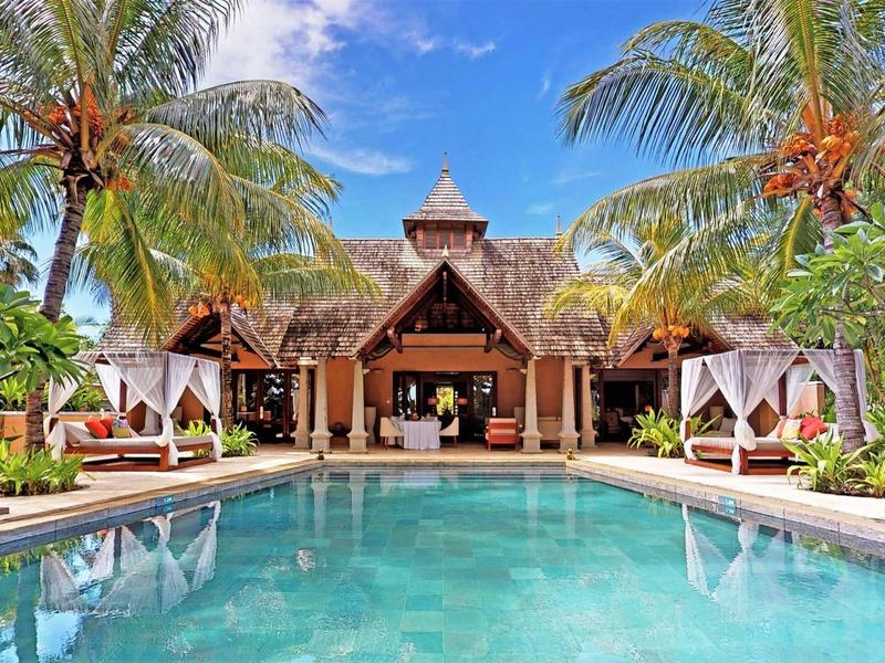 Luxury villa with palm trees and clear pool under blue sky in tropical vacation.