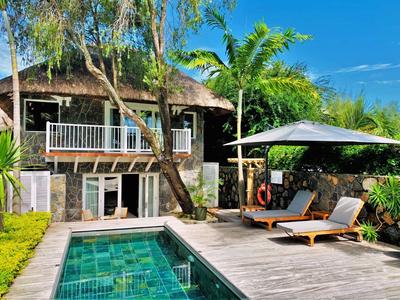 Piscina moderna con lettini e ombrellone accanto a una casa in un ambiente tropicale