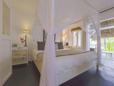 Camera luminosa con letto a baldacchino bianco e accesso a un balcone con vista verde.