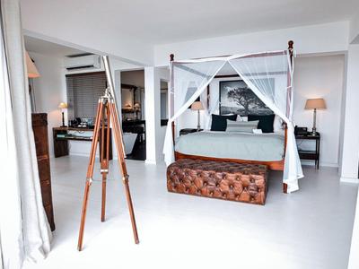 Camera d'hotel luminosa con letto a baldacchino, grande divano e arredamento moderno.