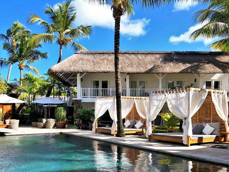 Resort di lusso con piscina, gazebo bianchi e palme sotto un cielo azzurro.