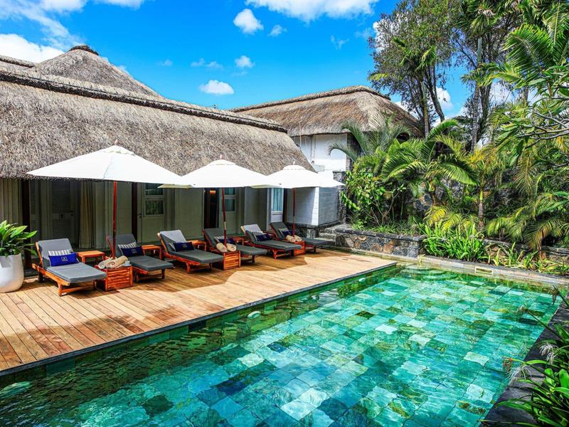 Resort di lusso con deck in legno, lettini, ombrelloni e piscina limpida in ambiente tropicale.