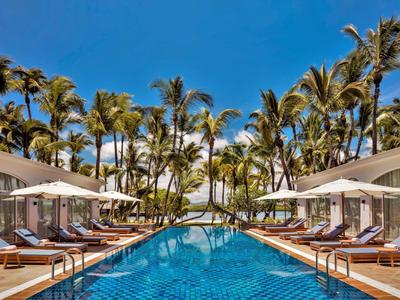 Großer Pool mit blauer Fliesenfläche, Liegestühlen und Palmen unter klarem Himmel.