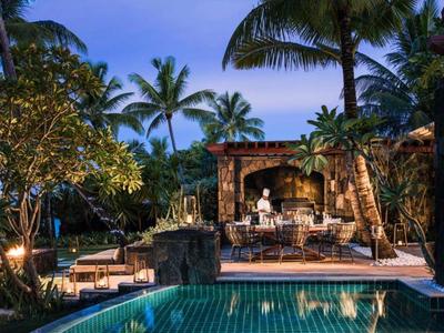 Lit pool area with seating and palm trees in a tropical hotel setting at dusk.