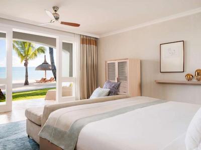 Modern hotel room with large bed, armchair, and view of the beach and sea.