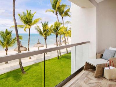 Balcony with glass railing overlooking a tropical beach with palm trees and ocean.