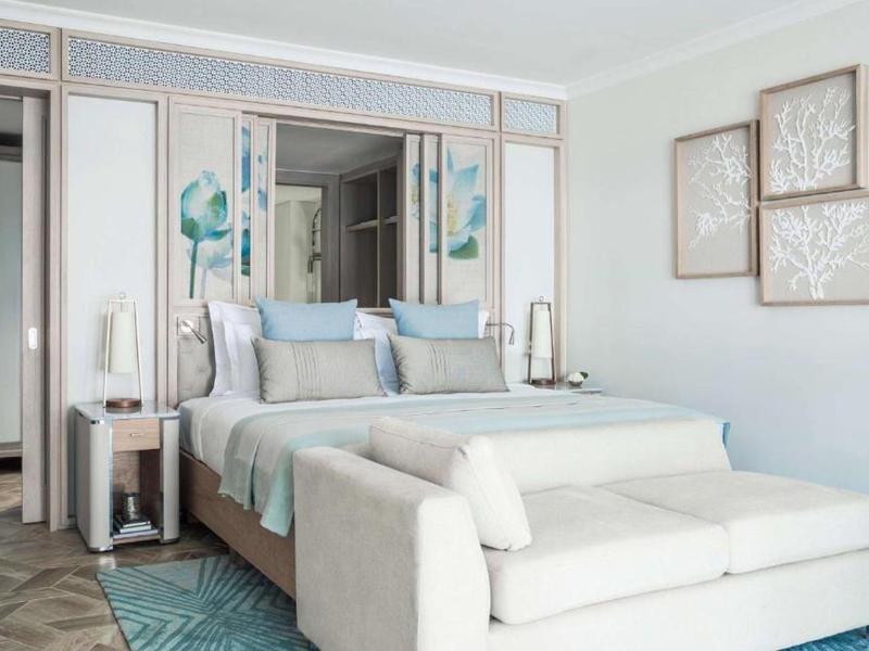 Modern hotel room with double bed, sofa, and soft blue and white tones.