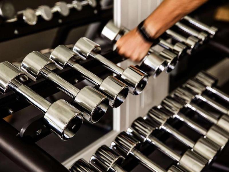 Row of shiny dumbbells in a gym with a hand grabbing one dumbbell.