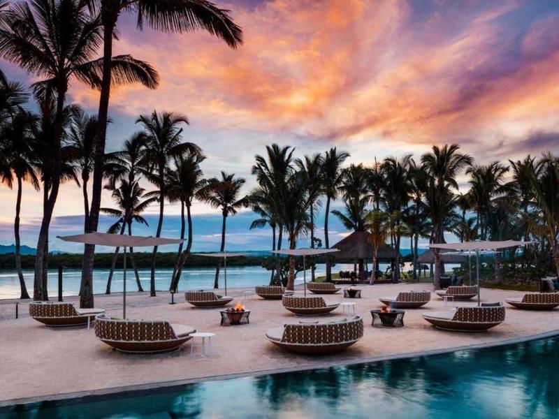 Pool area with lounge chairs and palm trees at sunset by the sea