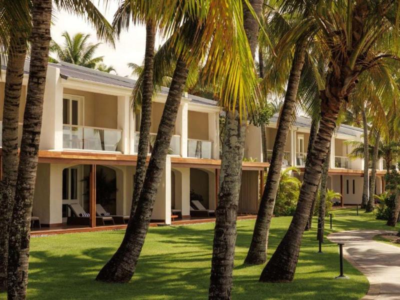 Hotel building with balconies surrounded by palm trees and well-kept lawn on a sunny day.