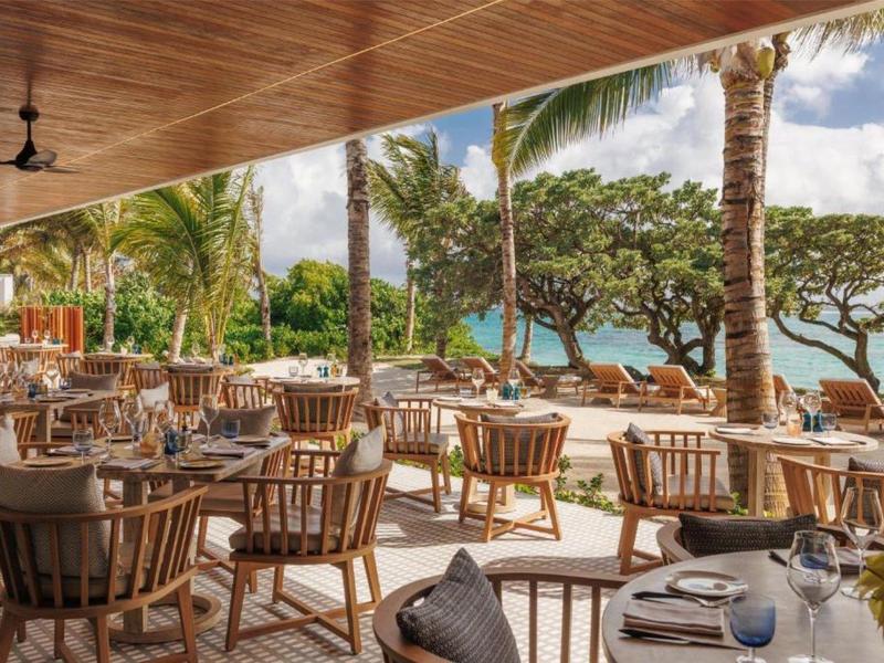 Open restaurant with wooden furniture overlooking palm trees and the sea.