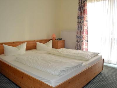 Hell eingerichtetes Schlafzimmer mit zwei Einzelbetten, weißen Bettdecken und bunten Vorhängen am Fenster.