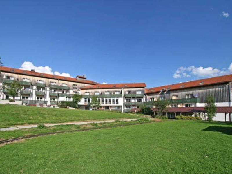 Großes weißes Gebäude mit rotem Dach auf einem grünen Rasen unter klarem blauem Himmel.