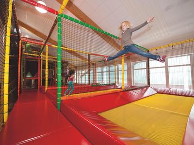 Kind springt im Trampolinbereich einer Indoor-Freizeitanlage mit roten und gelben Matten.