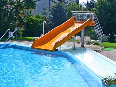 Ein Gartenpool mit oranger Wasserrutsche und grüner Umgebung bei sonnigem Wetter.