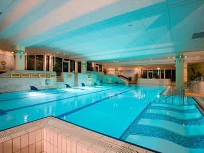 Piscina coperta con acqua illuminata e lettini in un hotel.