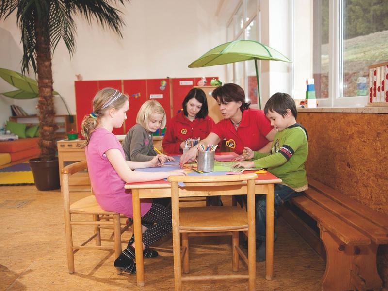 Fünf Kinder sitzen an einem Tisch und basteln in einem hellen Raum mit Pflanzen.