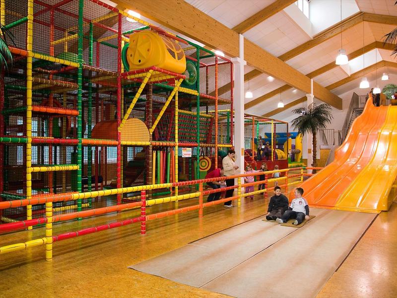 Indoor-Spielplatz mit Klettergerüst, Rutsche und zwei spielenden Kindern.