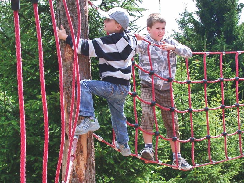Zwei Jungen klettern an einem Seilnetz im Freien, umgeben von grünen Bäumen.