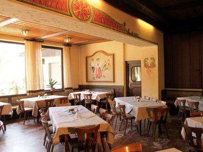 Hell beleuchteter Gastraum mit Holzstühlen und Tischen, weißen Tischdecken und Wandbildern.