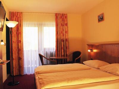 Gemütliches Hotelzimmer mit Doppelbett, Balkon, orangefarbenen Vorhängen und warmem Licht.