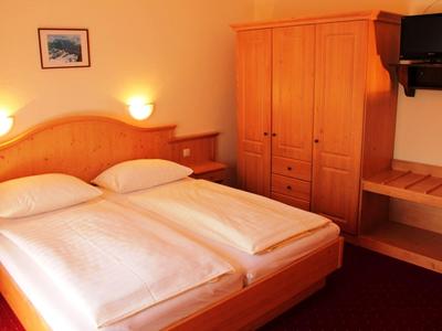 Gemütliches Schlafzimmer mit Doppelbett, Holzmöbeln und warmem Licht an hellen Wänden.