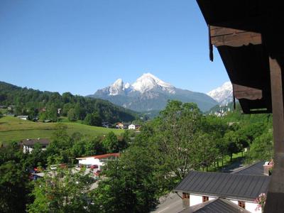 Blick von Balkon auf grüne Hügel, Bäume und schneebedeckten Berg unter klarem blauem Himmel.