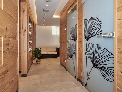 Heller Flur mit Holztüren und Glaswänden, dekoriert mit schwarzen Blattmustern, führt zu einem Wohnzimmer.