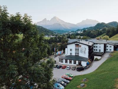 Hotelgebäude in einer grünen Berglandschaft mit Parkplatz und Bergen im Hintergrund