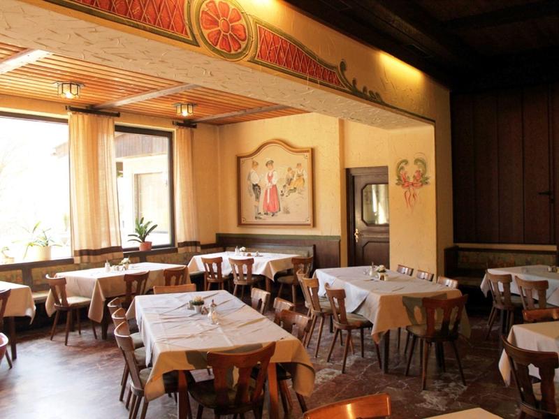 Hell beleuchteter Gastraum mit Holzstühlen und Tischen, weißen Tischdecken und Wandbildern.