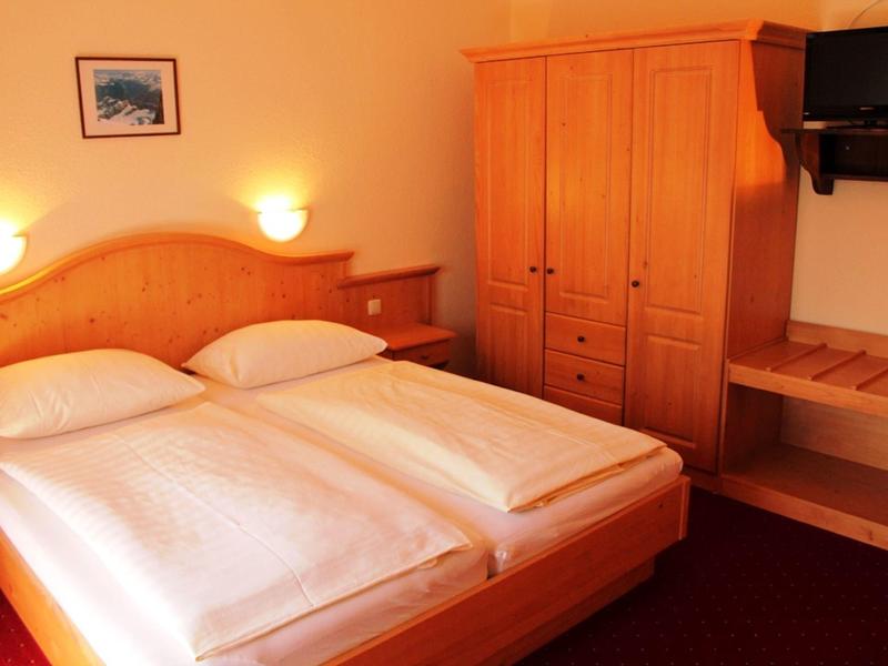 Gemütliches Schlafzimmer mit Doppelbett, Holzmöbeln und warmem Licht an hellen Wänden.