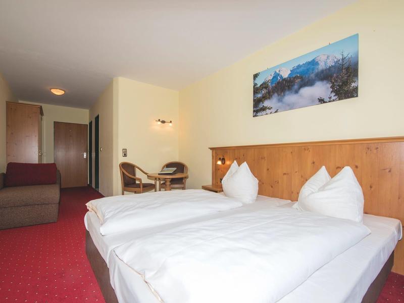 Hell eingerichtetes Hotelzimmer mit zwei Einzelbetten, Holzmöbeln und rotem Teppichboden.