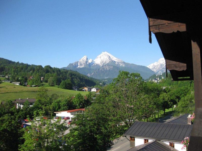 Blick von Balkon auf grüne Hügel, Bäume und schneebedeckten Berg unter klarem blauem Himmel.