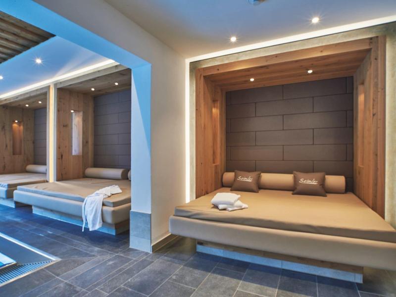 Modernes Spa mit bequemen Holzliegen, indirekter Beleuchtung und blauem Pool im Vordergrund.