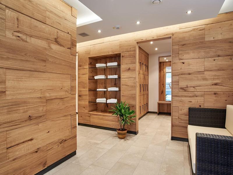 Moderner Flur mit hellen Holzpaneelen, weißem Boden, integriertem Regal und einem kleinen grünen Pflanze.