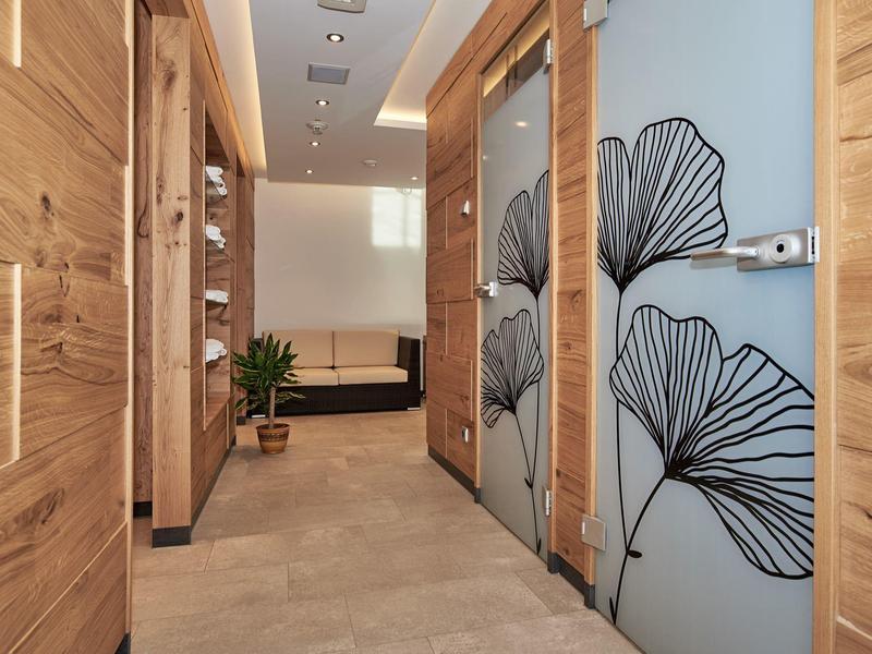 Heller Flur mit Holztüren und Glaswänden, dekoriert mit schwarzen Blattmustern, führt zu einem Wohnzimmer.