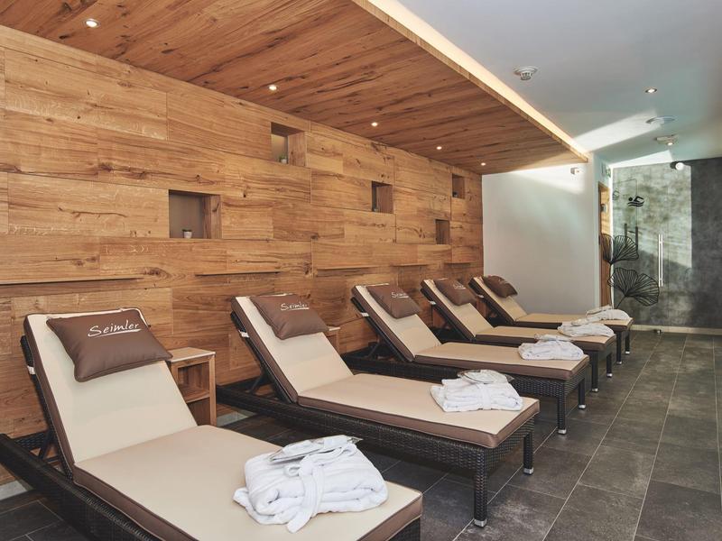 Moderne Wellness-Liegeflächen mit Holzwand und schwarzen Kissen in hellem, ruhigem Raum.