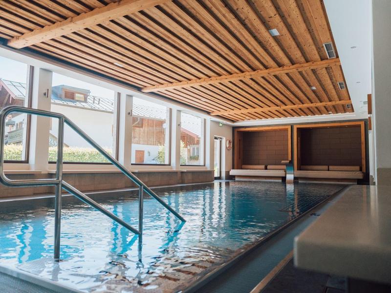 Moderner Innenpool mit Holzlamellendecke, großen Fenstern und Metallleiter.