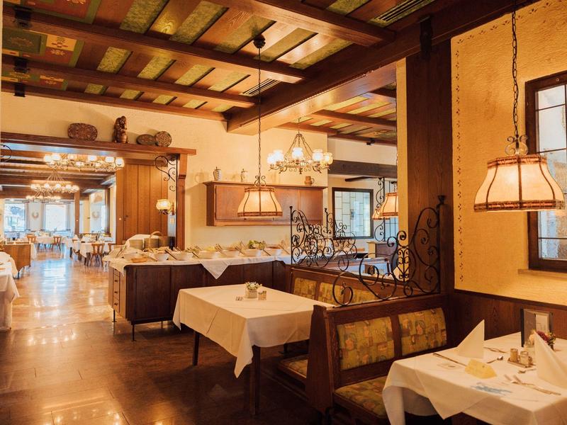 Gemütliches Restaurant mit Holzbalkendecke, warmem Licht und gedeckten Tischen mit weißen Tischdecken.